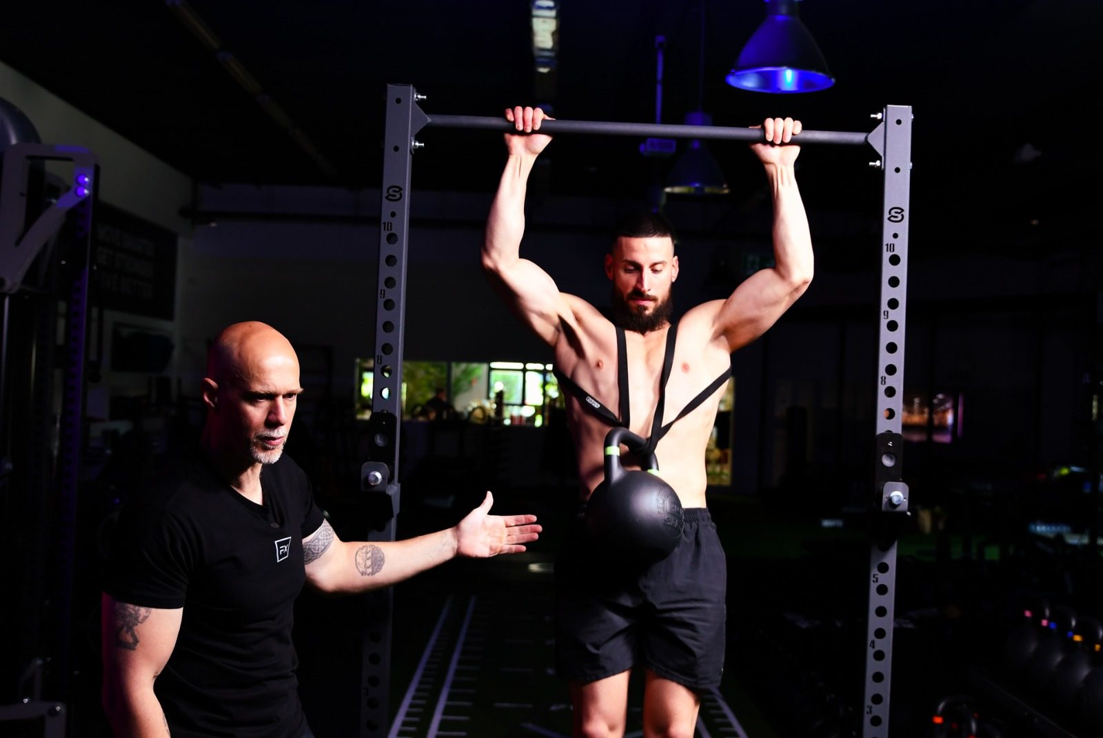 Trazioni alla sbarra con una kettlebell come sovraccarico, sotto lo sguardo del docente